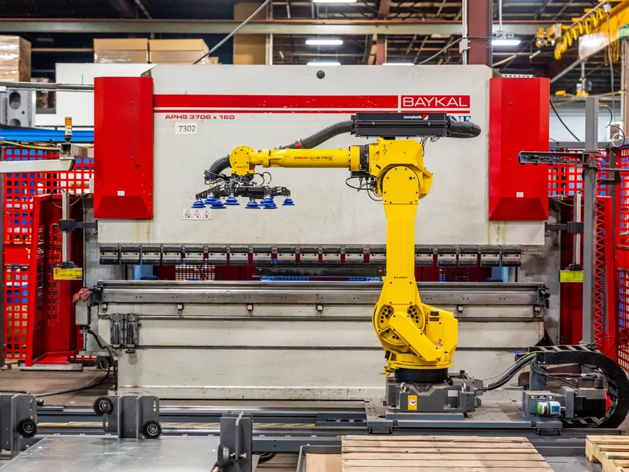 The FANUC M-710iC/70 on its rail, side-on to the Baykal press brake, with the vacuum gripper lowered toward the brake bed