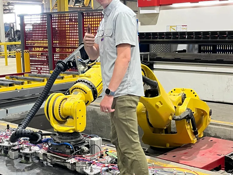 A technician beside a FANUC robot with vacuum bar tooling in front of a press brake