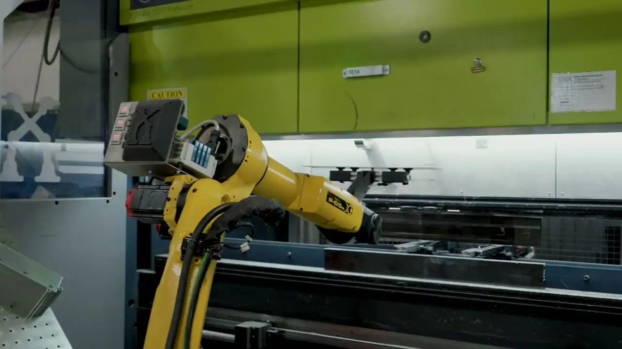 A FANUC robot with a gripper places a formed part at a green press brake inside a TWA cell
