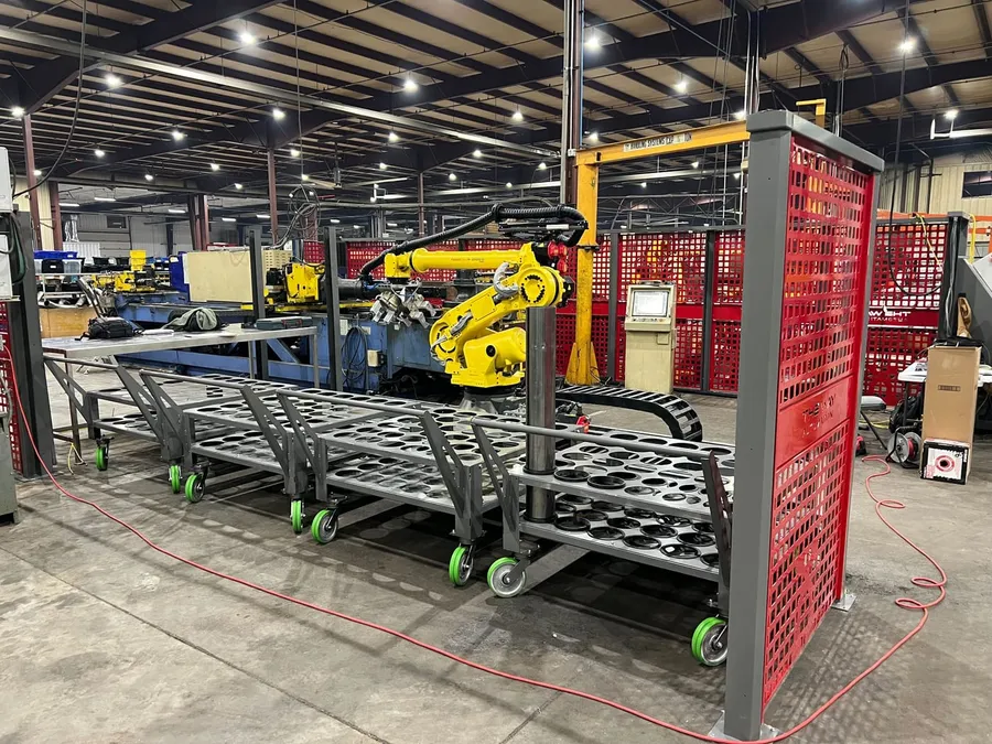 The robot on its rail beside the bender, with the infeed carts of tube stock docked inside the cell