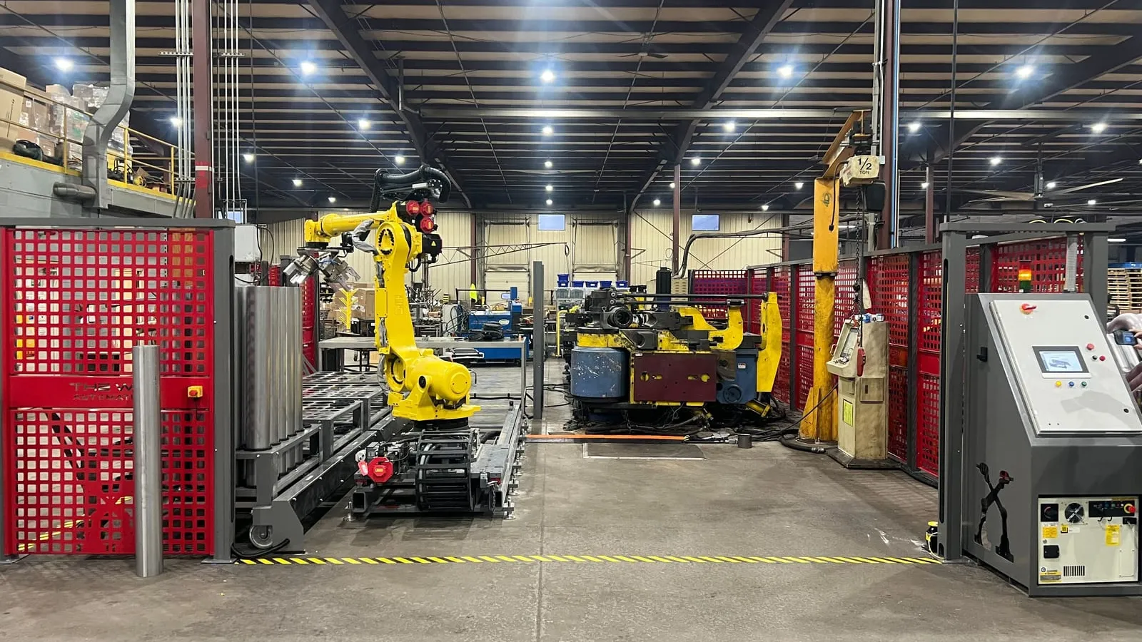 A FANUC robot on a linear rail tending a CNC tube bender inside a fenced TWA cell