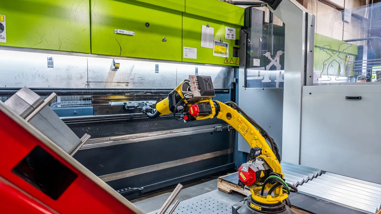 FANUC robot arm tending a press brake with finished sheet-metal parts stacked beside it