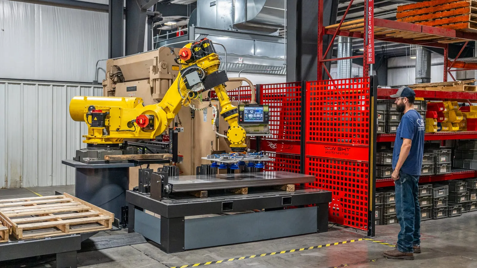 A representative TWA handling cell: a FANUC robot with a vacuum gripper lowering a steel plate onto a pallet station. The customer's floor is not shown.