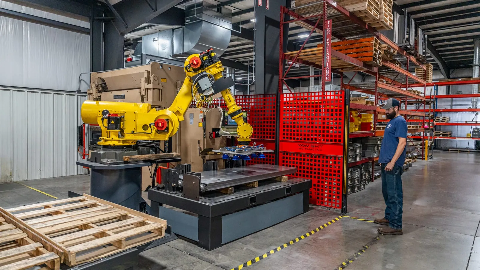 A FANUC robot with a vacuum end effector loading sheet-metal blanks at a press brake in a TWA cell