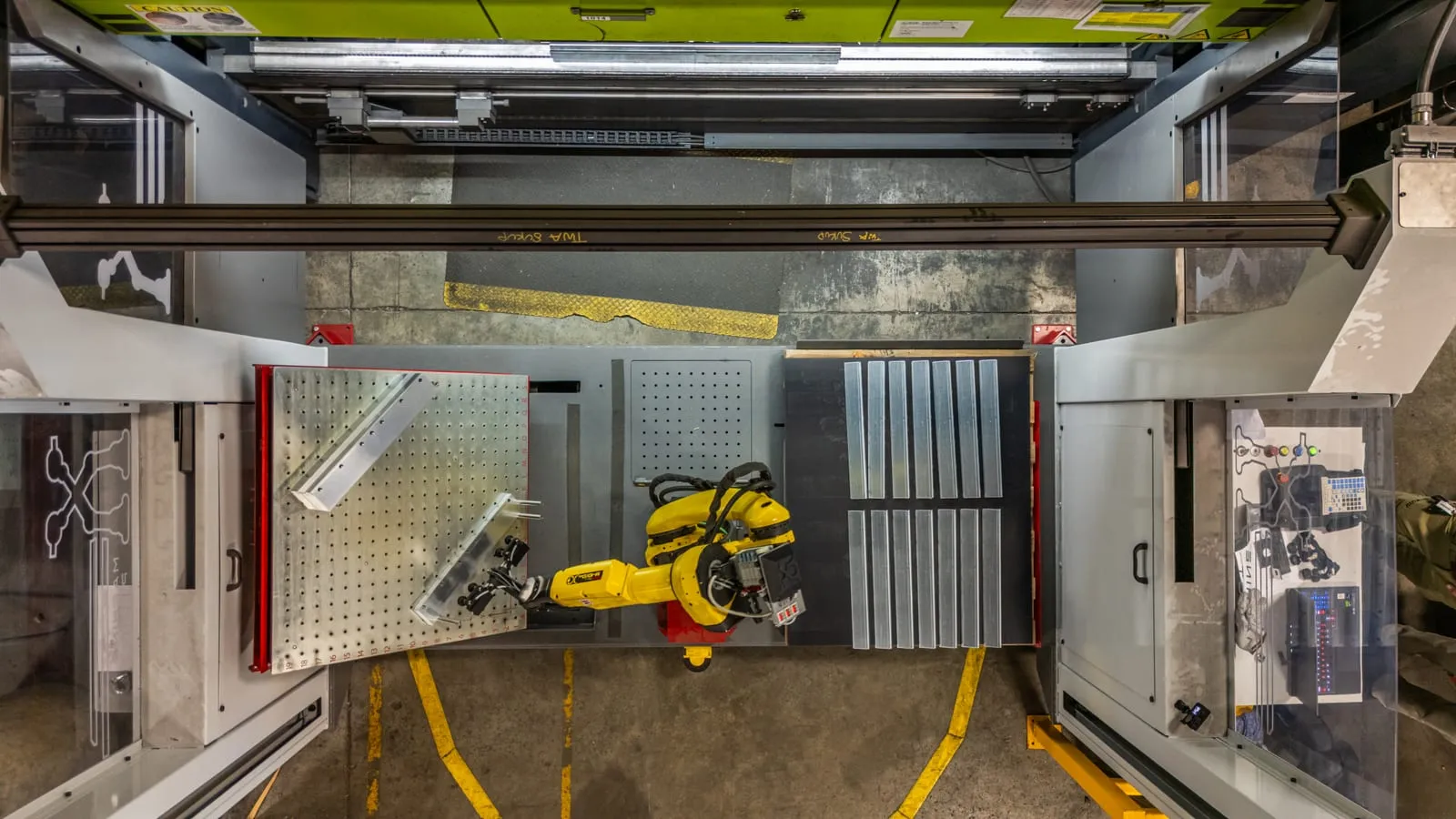 Overhead view of a FANUC robot on a rail serving two machines inside a fenced TWA cell