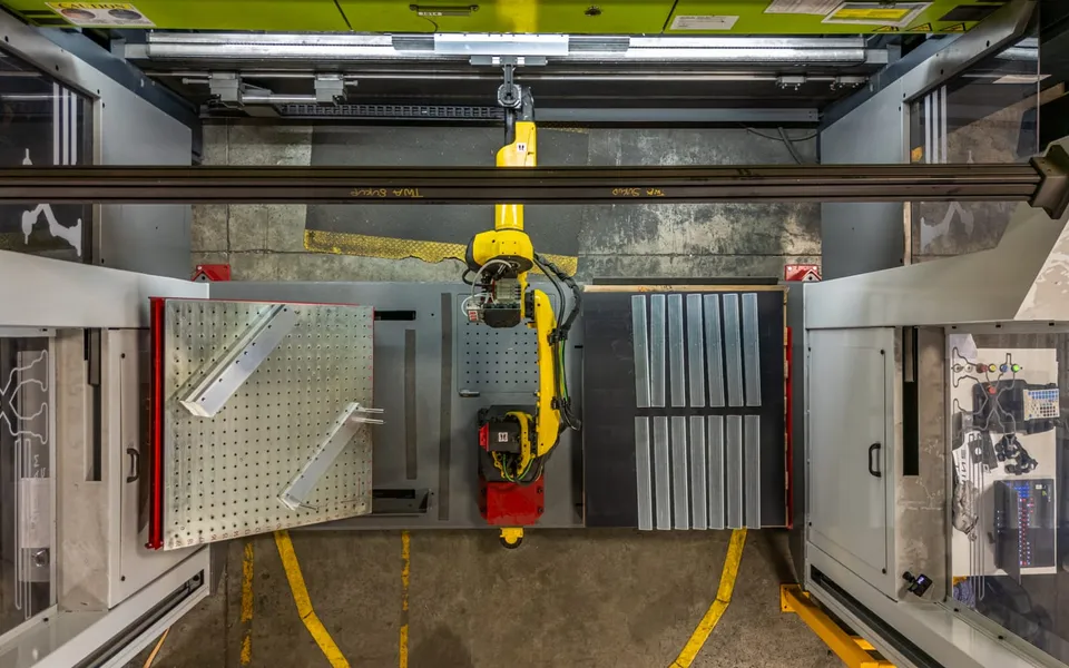 A FANUC robot on a rail between two enclosed machines in the press-tending cell, seen from above