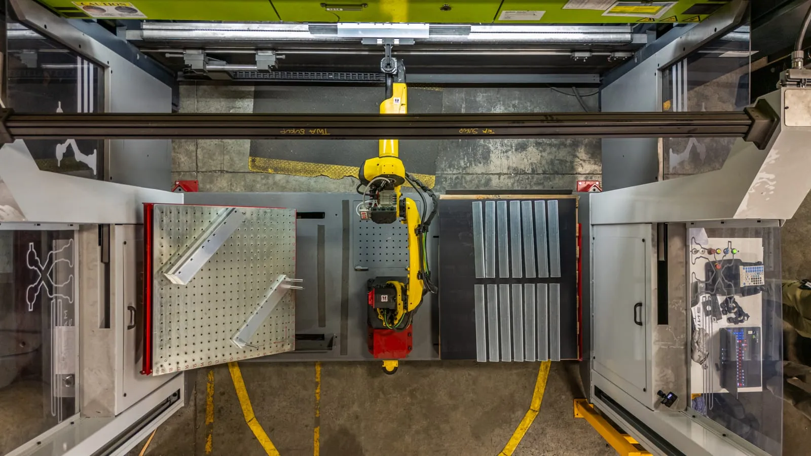 A FANUC robot on a rail between two enclosed machines in the press-tending cell, seen from above