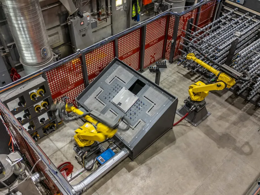 Overhead view of the two robots handling panels beside the part racks inside the fenced cell