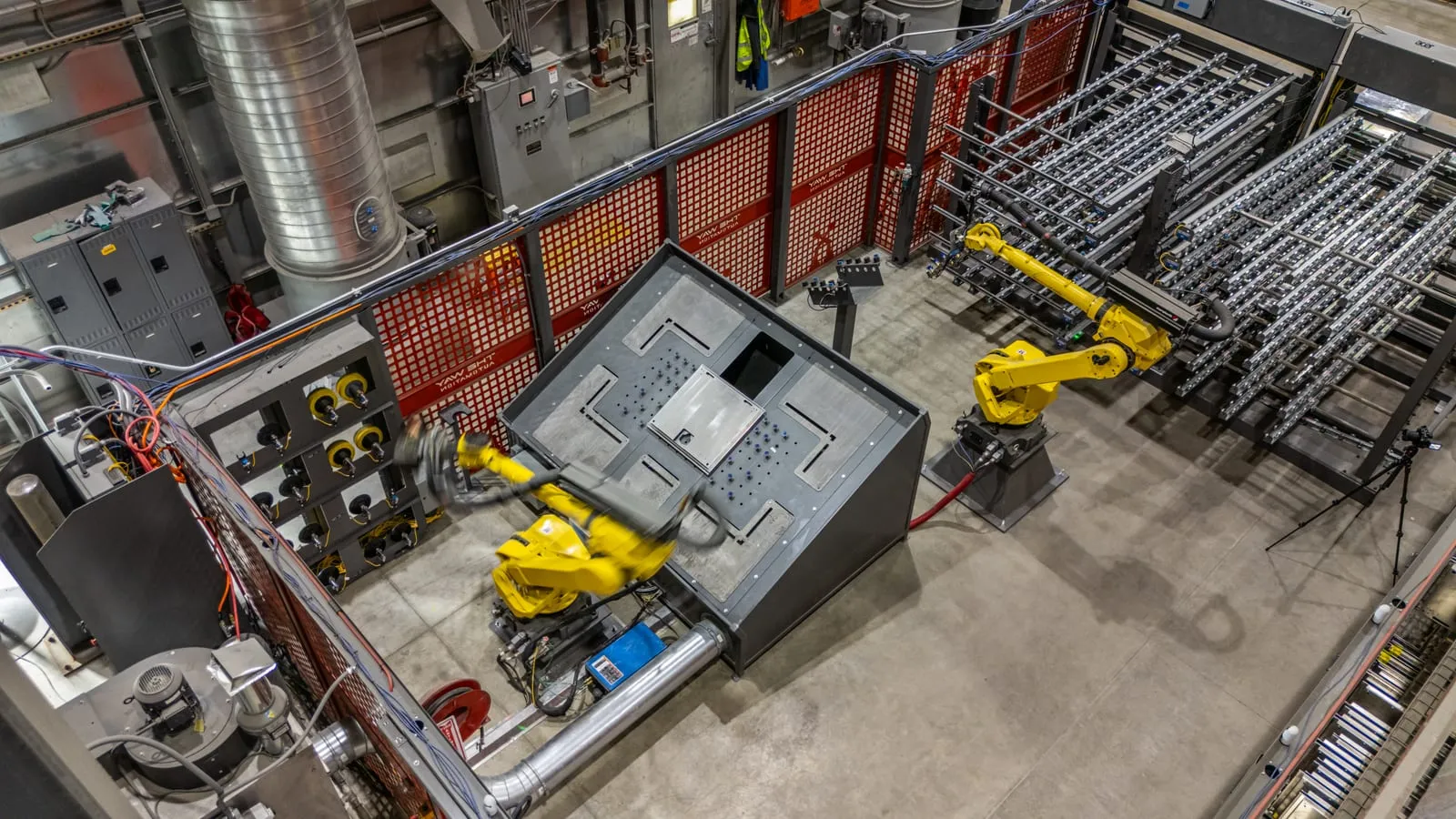 Overhead view of two FANUC robots handling sheet-metal panels beside part racks inside the finishing cell