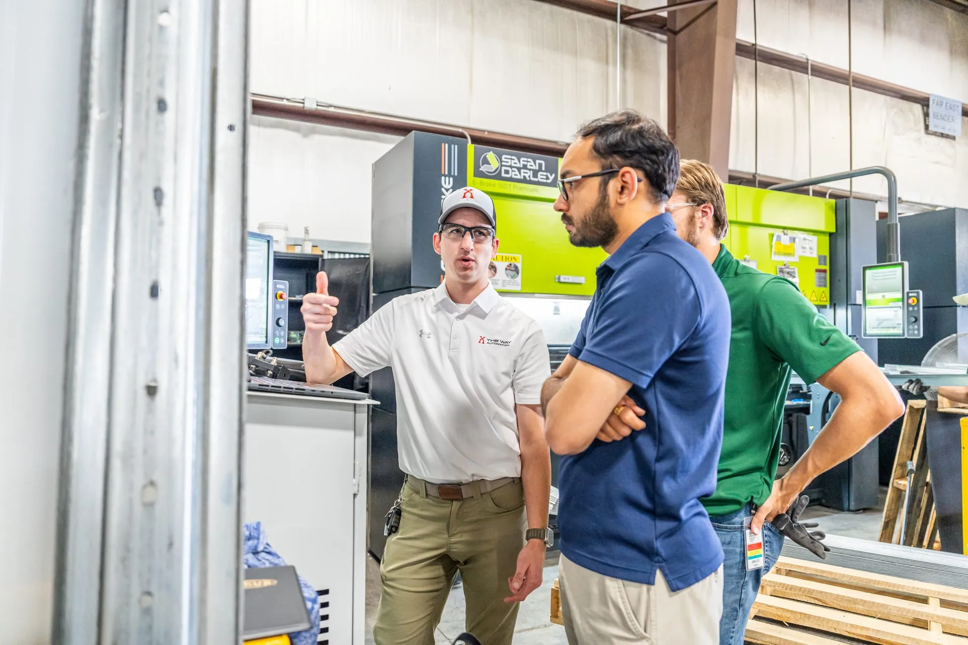 Three men talk on a shop floor in front of a press brake