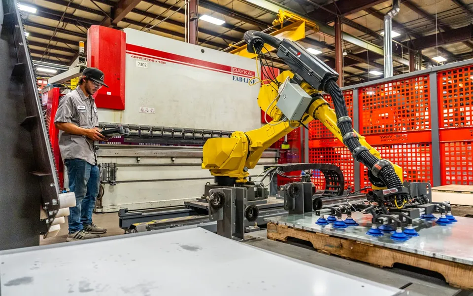 A TWA technician at the teach pendant beside a robot on a rail at a press brake