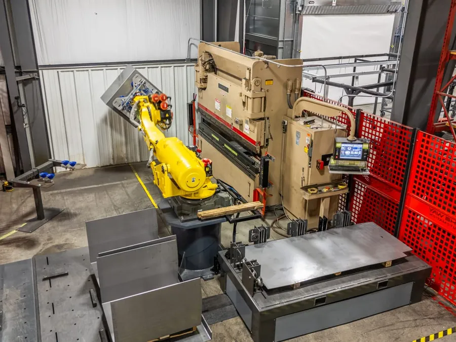 The robot holding a sheet-metal blank in front of the press brake inside the fenced cell