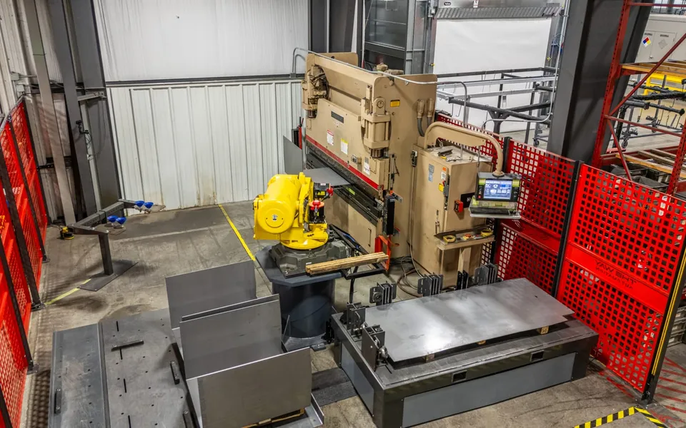 The FANUC R-2000iB/200R inside the fenced Thunder Creek cell, tending the Cincinnati press brake with sheet-metal blanks staged beside it