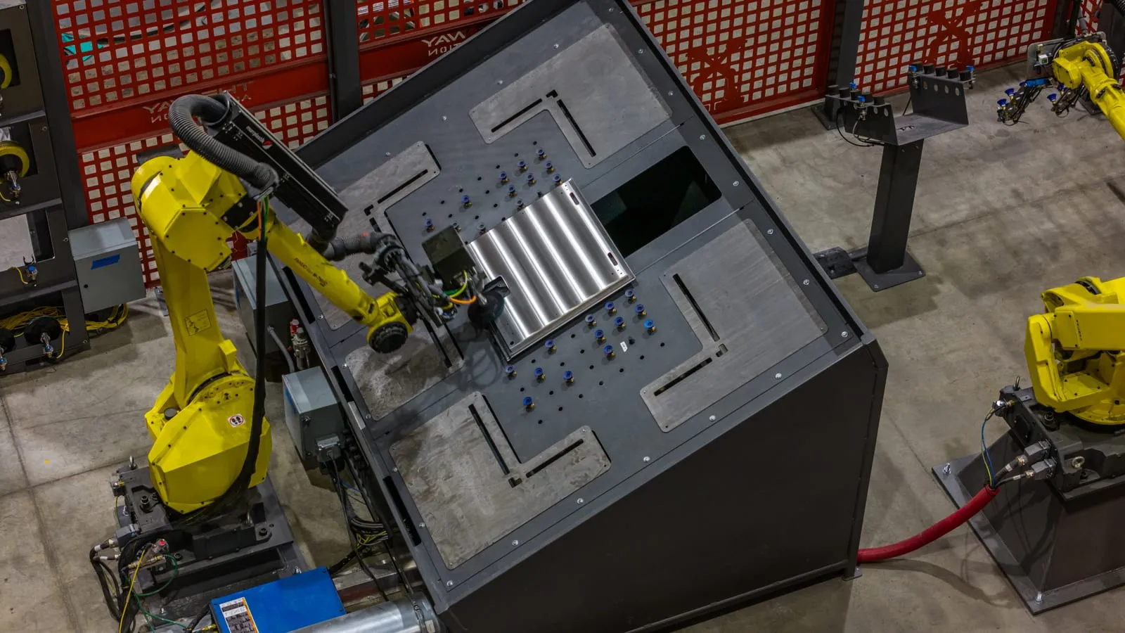 A FANUC robot with a welding torch at a fixture table inside a curtained weld cell